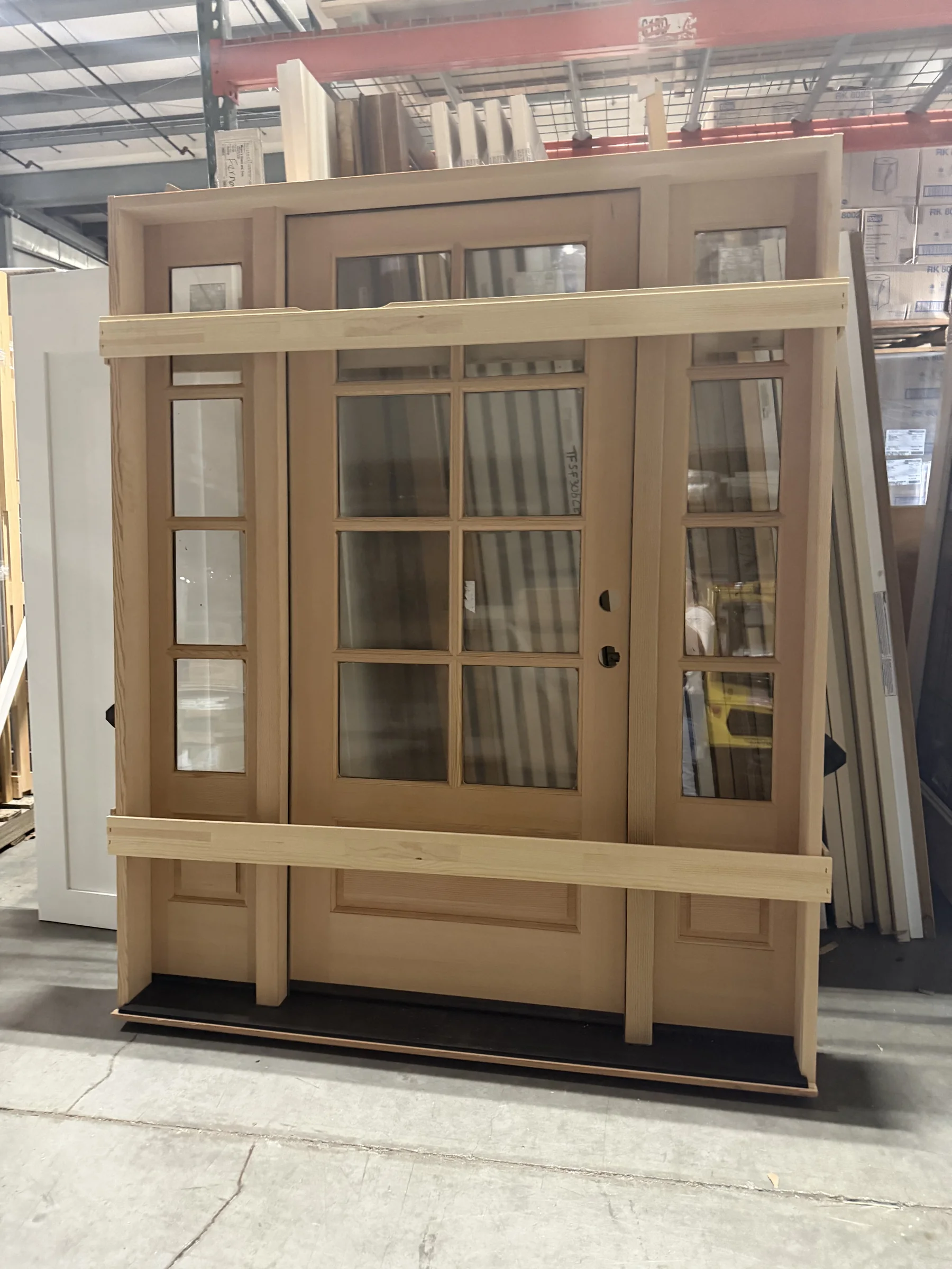Large custom wood door unit with glass panels, sidelights, and upper transoms inside the Moore's Doors warehouse