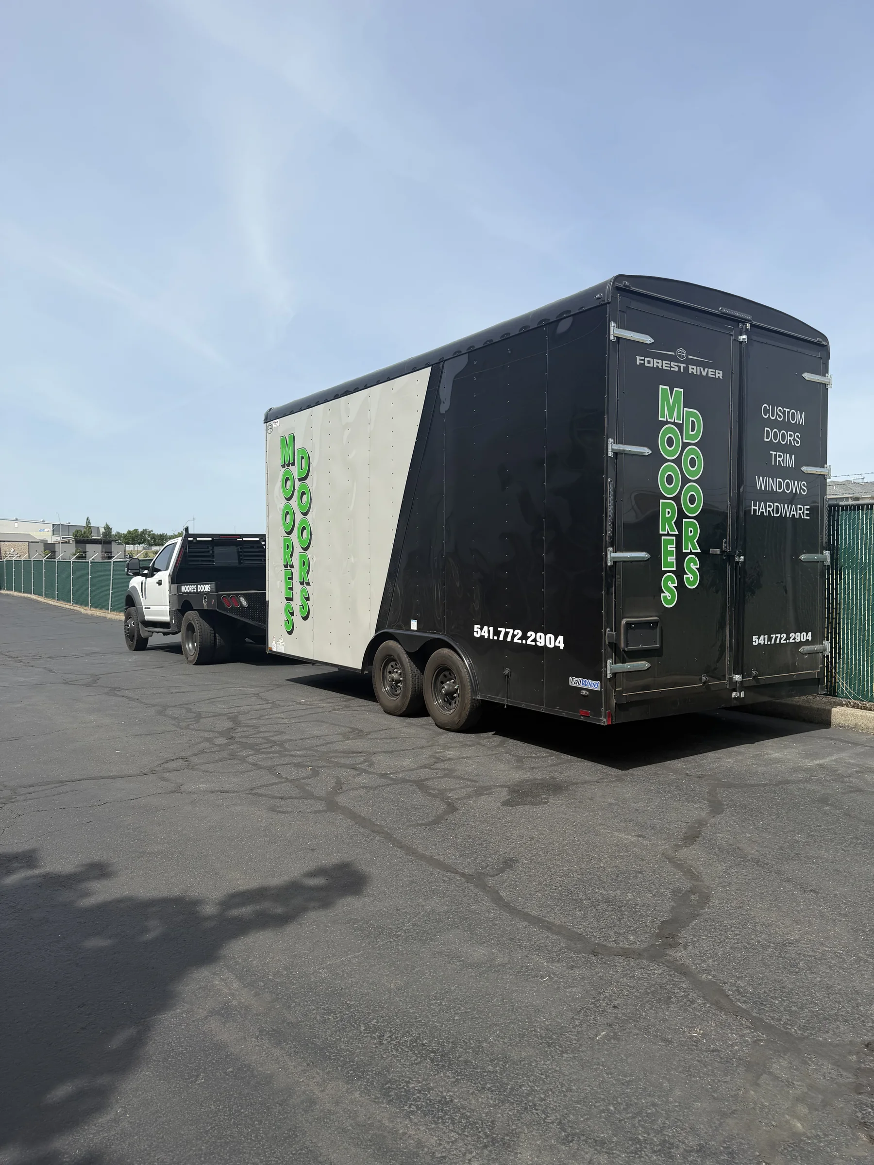 Black Moore's Doors pickup and enclosed branded trailer parked outside