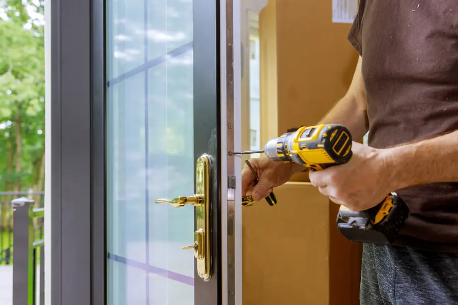 Close-up of a brass entry door handle and lock being adjusted with a cordless drill
