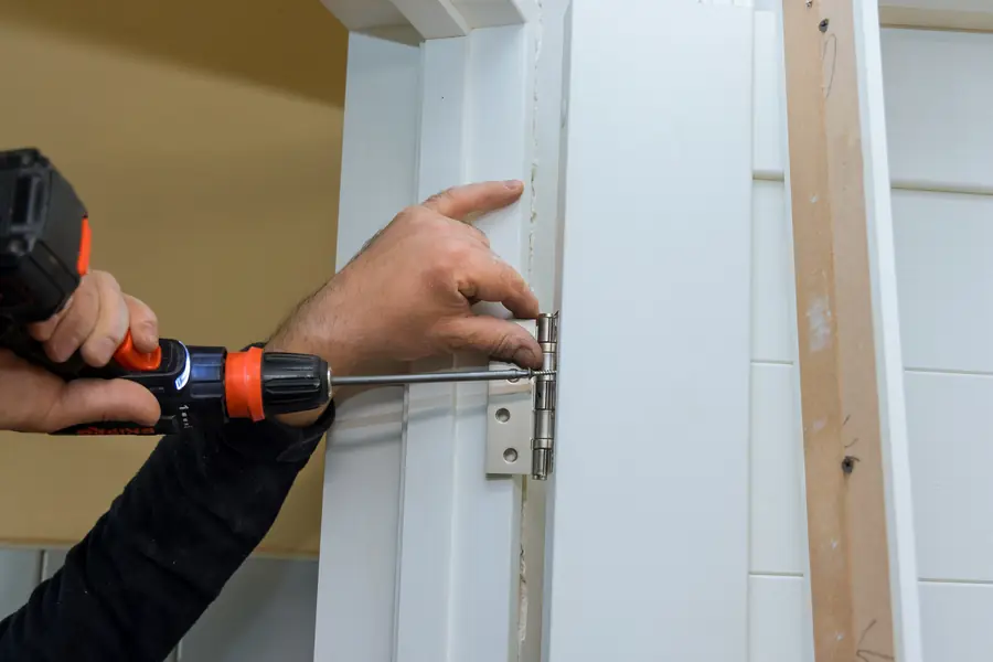 Close-up of a hinge recess being prepared on the edge of a white door with a cordless drill