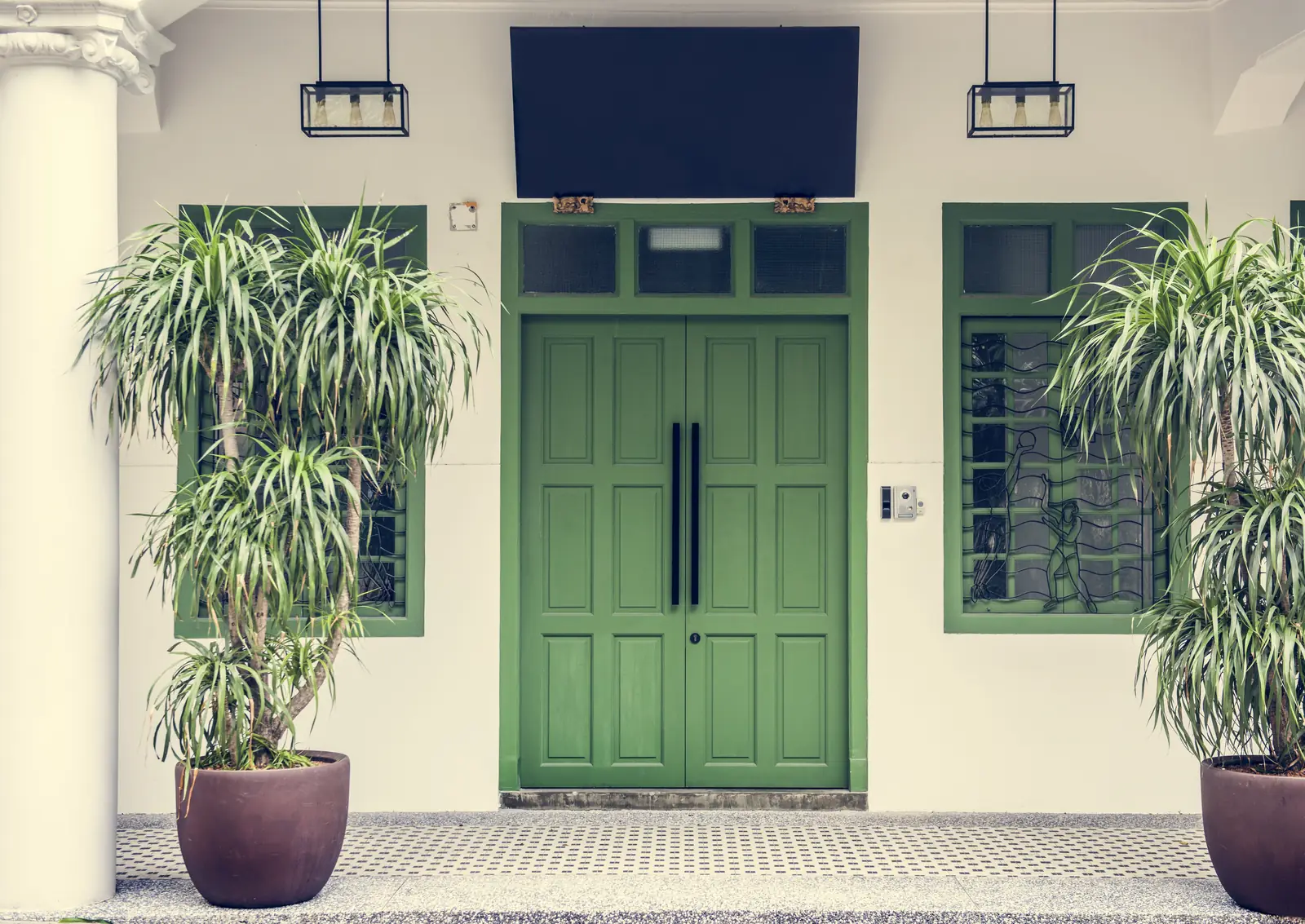 Green double entry doors with matching sidelights framed by two potted plants