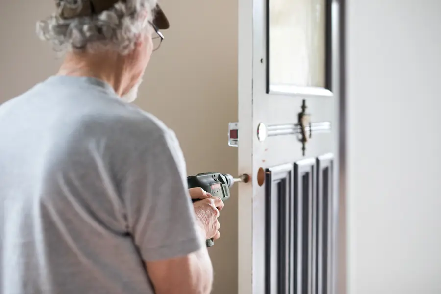 Person preparing the lock area on a dark interior door with a cordless drill