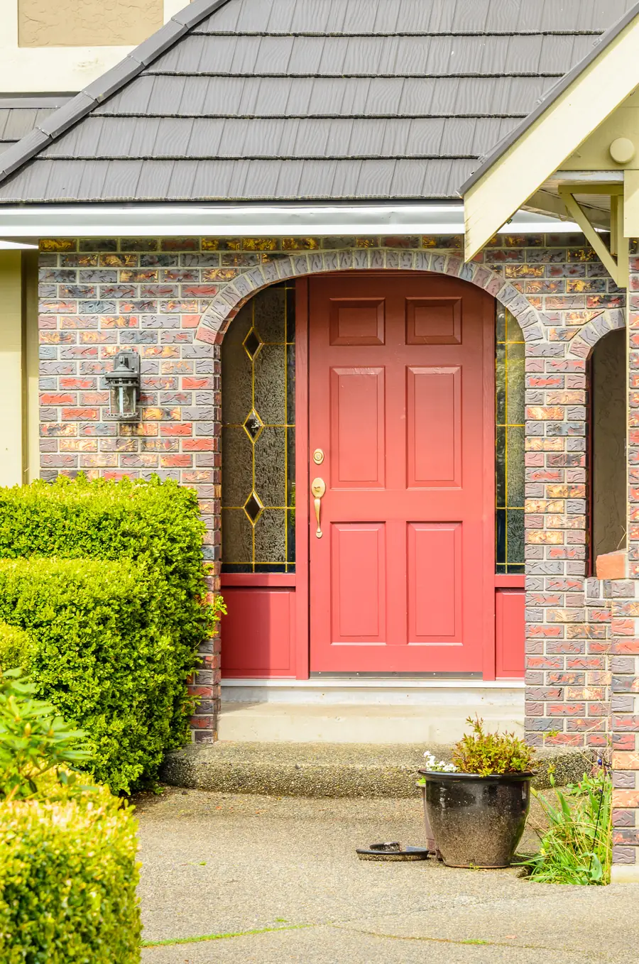 Red arched front door centered on a brick home with shrubs and a concrete walkway